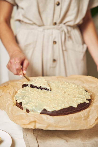 Giovane cuoca che prepara una deliziosa torta al cioccolato con crema su un tavolo bianco