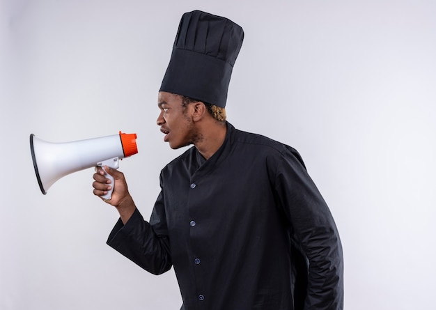 Giovane cuoco afro-americano in uniforme da chef tiene altoparlante e guarda al lato isolato su sfondo bianco con spazio di copia