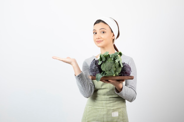 Giovane cuoco che tiene piatto di cavolo e broccoli e mostra uno spazio aperto