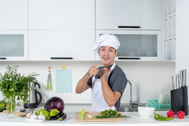 Giovane cuoco di vista frontale in uniforme che indica alla macchina fotografica