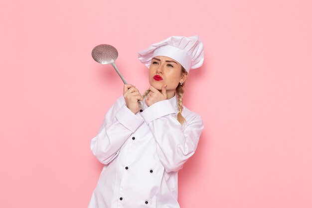 Giovane cuoco femminile di vista frontale in vestito bianco che tiene cucchiaio d'argento sullo spazio rosa cucinare cucina lavoro lavoro foto