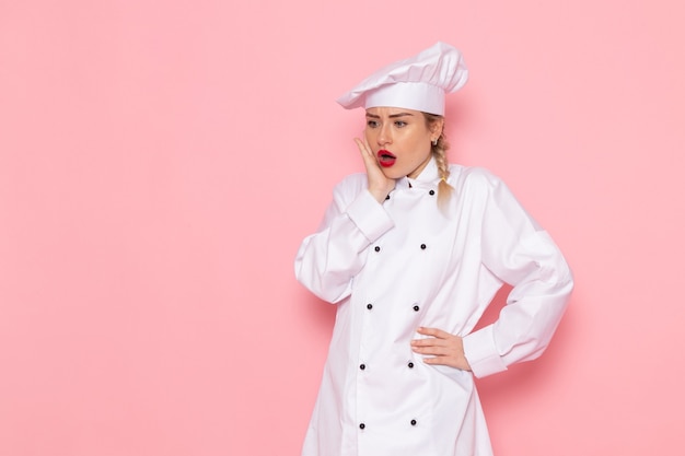Giovane cuoco femminile di vista frontale in vestito bianco del cuoco che posa con l'espressione sorpresa sulla foto del lavoro di lavoro di cucina del cuoco dello spazio rosa