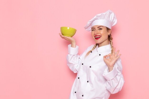 Giovane cuoco femminile di vista frontale in vestito bianco del cuoco che sorride e che tiene piatto verde sul cuoco rosa dello spazio