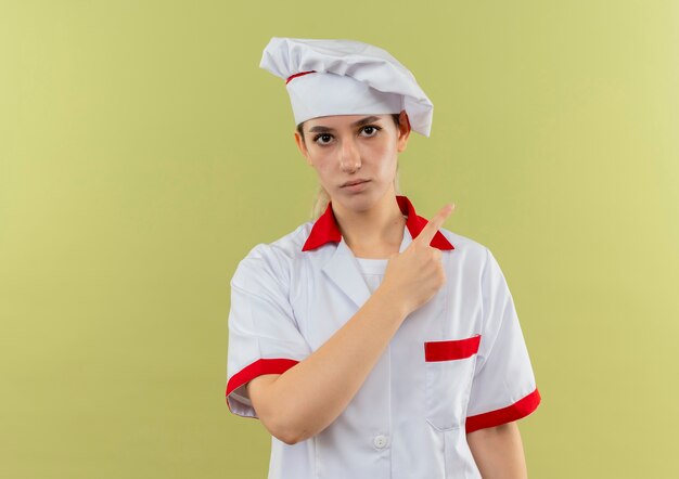 Giovane cuoco grazioso in uniforme del cuoco unico che indica alla ricerca laterale