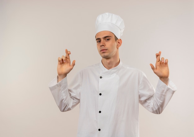 giovane cuoco maschio che indossa le dita incrociate uniforme dello chef sul muro bianco isolato con lo spazio della copia