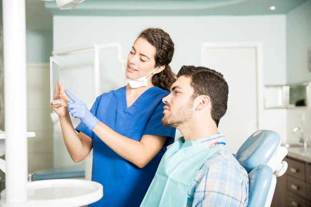 Giovane dentista che mostra la tavoletta digitale al paziente maschio durante il trattamento in clinica odontoiatrica