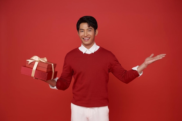 Giovane di etnia asiatica indossa un maglione rosso tiene una scatola regalo rossa con un fiocco di nastro regalo