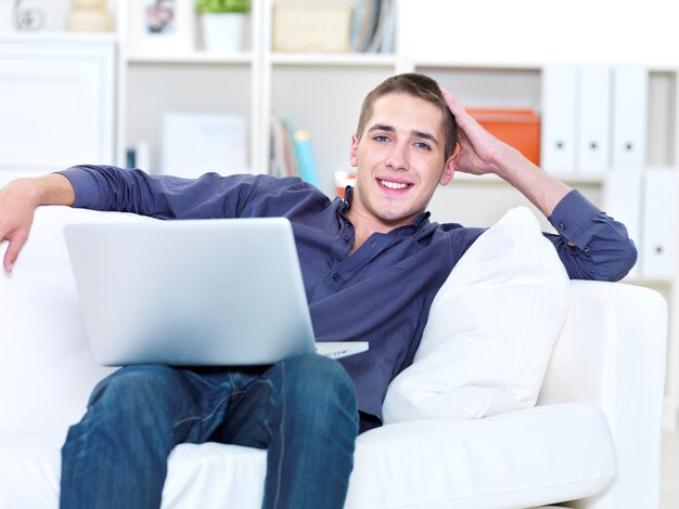Giovane di felicità con il computer portatile e sdraiato sul divano