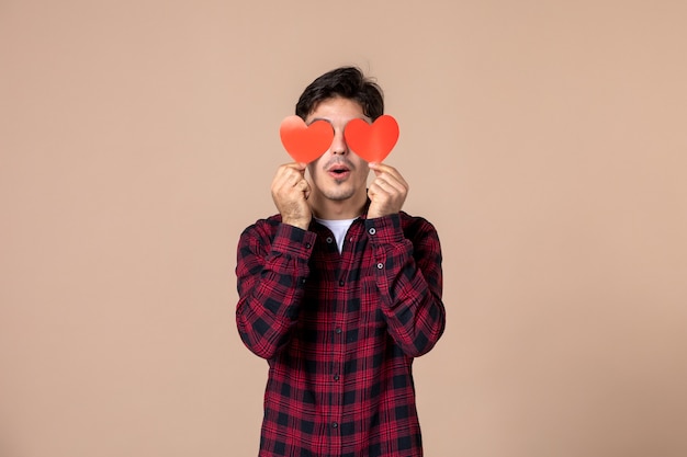 Giovane di vista frontale che tiene gli adesivi del cuore rosso sulla parete marrone