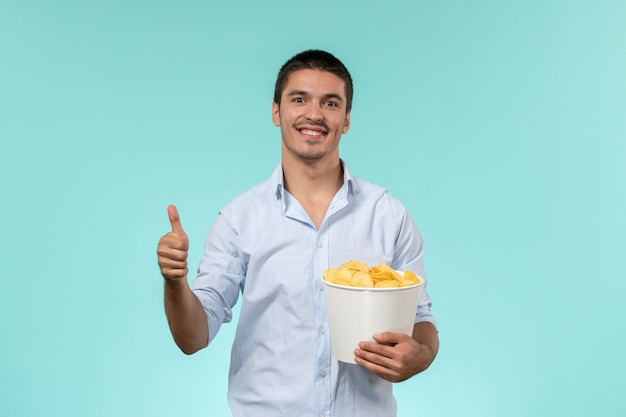 Giovane di vista frontale che tiene le patatine fritte con il sorriso su un cinema maschio remoto solitario della parete blu