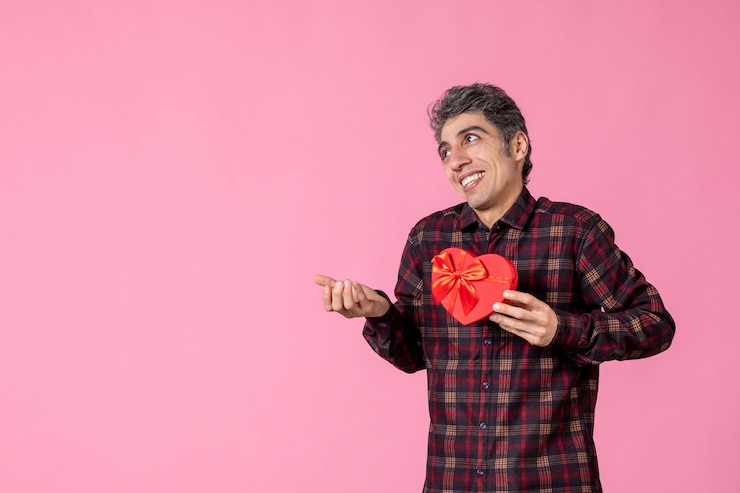 Foto gratuito giovane di vista frontale che tiene presente a forma di cuore rosso sulla parete rosa