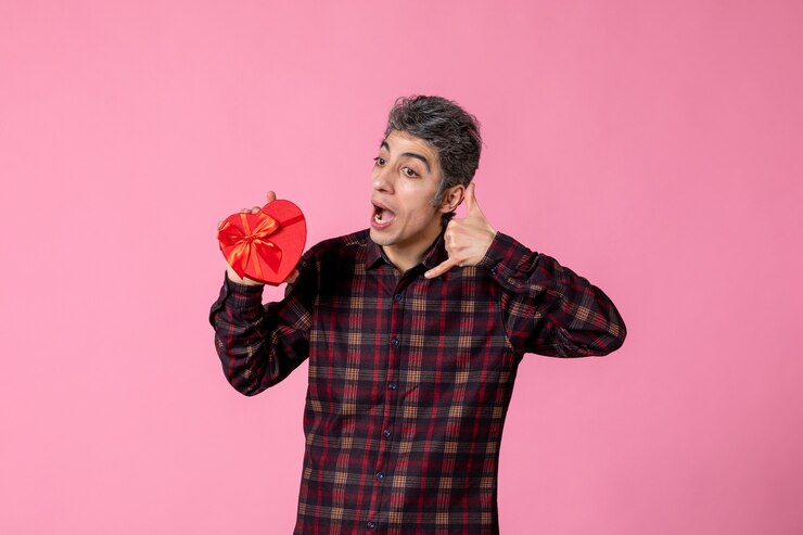 Foto gratuito giovane di vista frontale che tiene presente a forma di cuore rosso sulla parete rosa