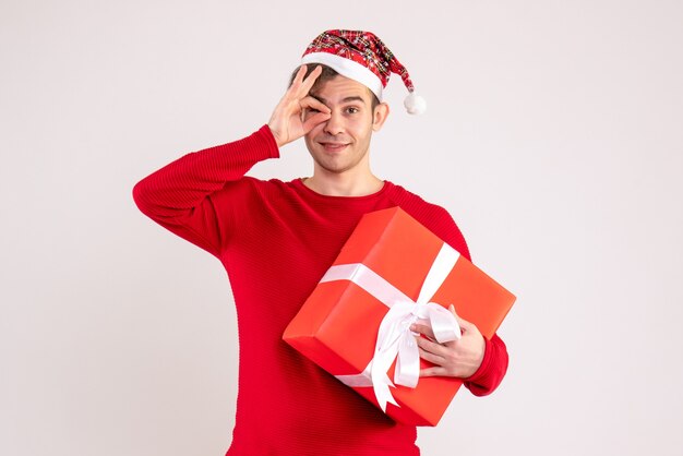 Giovane di vista frontale con il cappello della Santa che mette il segno okey davanti ad un occhio su fondo bianco