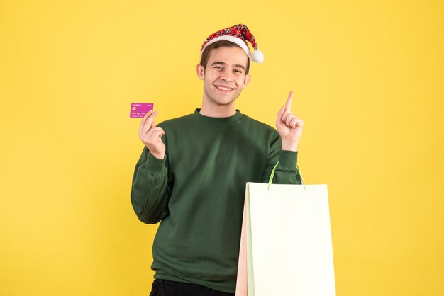 Giovane di vista frontale con il cappello della Santa che tiene i sacchetti della spesa e la carta che stanno sullo spazio giallo della copia del fondo