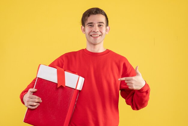 Giovane di vista frontale con il maglione rosso che indica il suo regalo su priorità bassa gialla