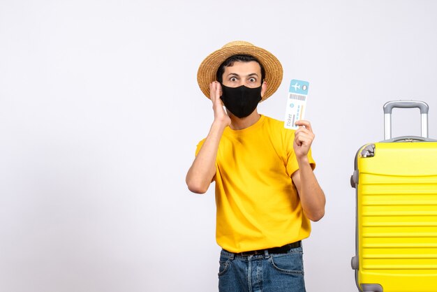 Giovane di vista frontale con la maglietta gialla che sta vicino alla valigia gialla che sostiene il biglietto di viaggio