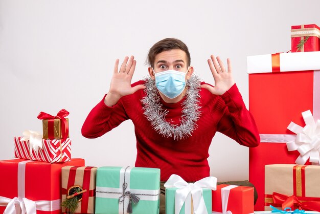 Giovane di vista frontale con la maschera che apre le mani che si siedono intorno ai regali di natale