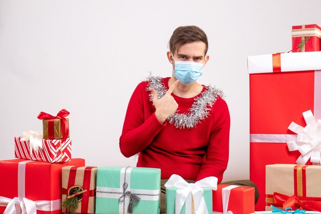 Giovane di vista frontale con la maschera che indica alla maschera che si siede intorno ai regali di natale