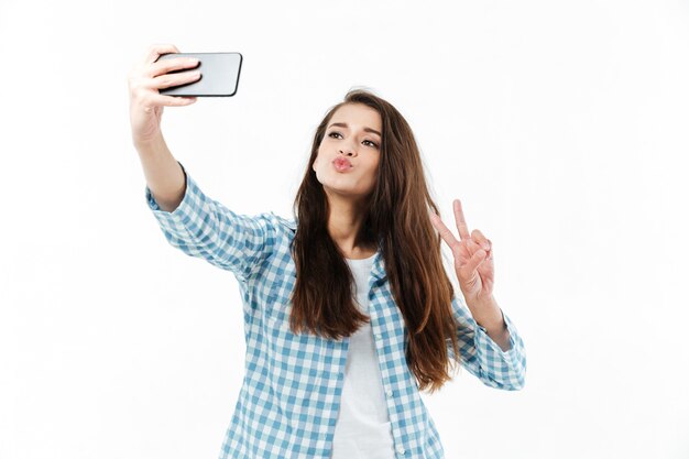 Giovane donna abbastanza adorabile che fa selfie e che mostra gesto di vittoria