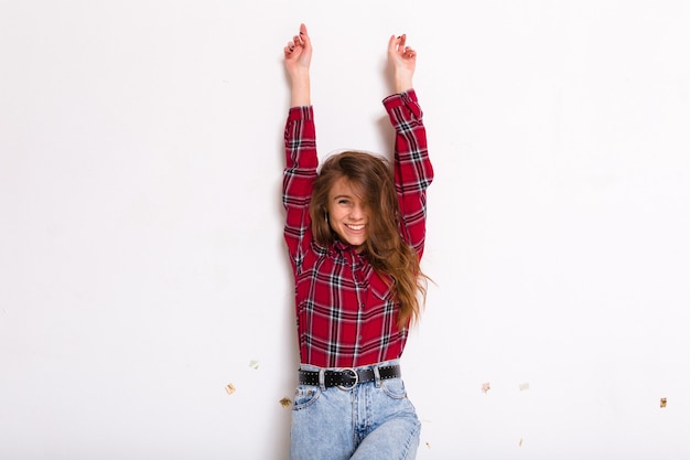 Giovane donna abbastanza affascinante con capelli lunghi che posano con le mani in alto e sorridono indossando la camicia rossa su bianco