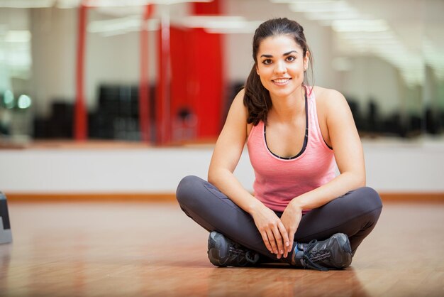 Giovane donna abbastanza ispanica che si siede e che aspetta la sua lezione di ginnastica