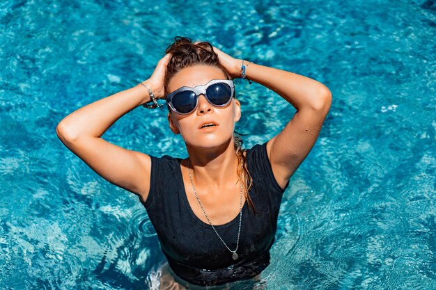 giovane donna abbronzata in occhiali da sole in piscina, moda, schizzi.