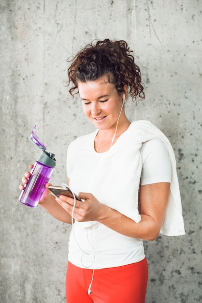 Giovane donna adatta con la bottiglia di acqua facendo uso del cellulare