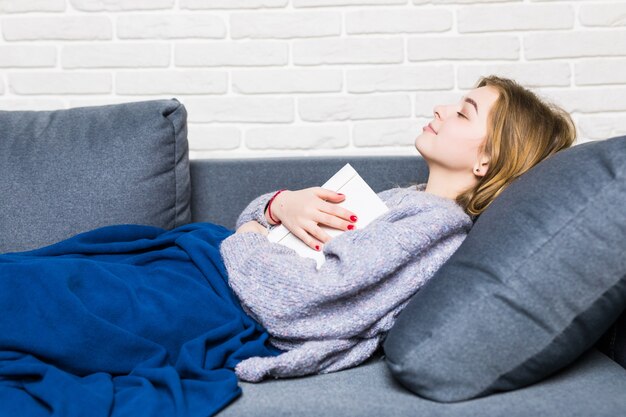 Giovane donna addormentata durante la lettura sdraiata sulla schiena nel letto con il suo libro appoggiato sullo stomaco