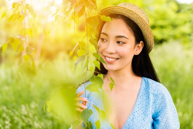 Giovane donna affascinante che sorride mentre appoggiandosi alle foglie in natura