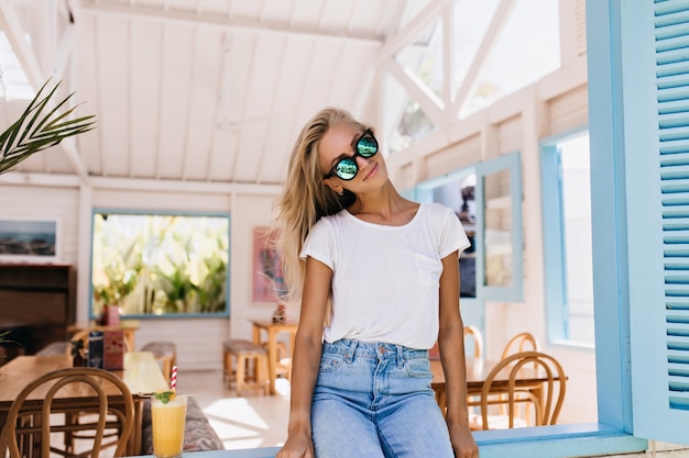 Giovane donna affascinante in blue jeans che si siede sul davanzale della finestra.