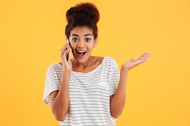 Giovane donna africana felice con la bocca aperta che parla sul telefono isolato