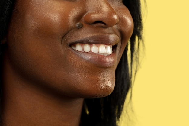 Giovane donna afro-americana isolata sulla parete gialla, espressione facciale. Il sorriso della bella femmina si chiuda sul ritratto. Concetto di emozioni umane, espressione facciale.