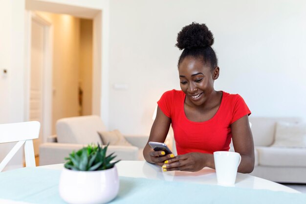 Giovane donna afroamericana che beve caffè e chiacchiera con gli amici sui social network con il suo telefono cellulare