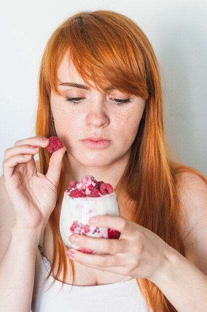 Giovane donna aggiungendo il lampone nel bicchiere di yogurt
