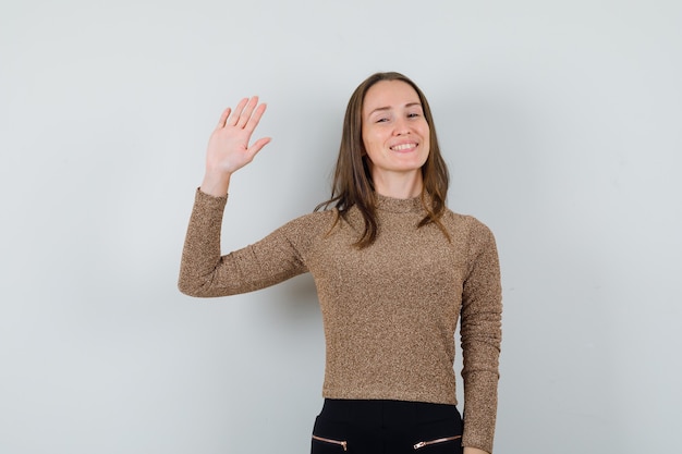 Giovane donna agitando la mano per addio in camicetta dorata e guardando concentrato