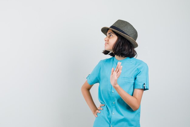 Giovane donna agitando la mano per addio in camicia blu, cappello