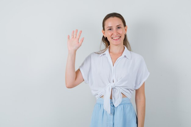 Giovane donna agitando la mano per il saluto in camicetta e gonna e sembra gioviale