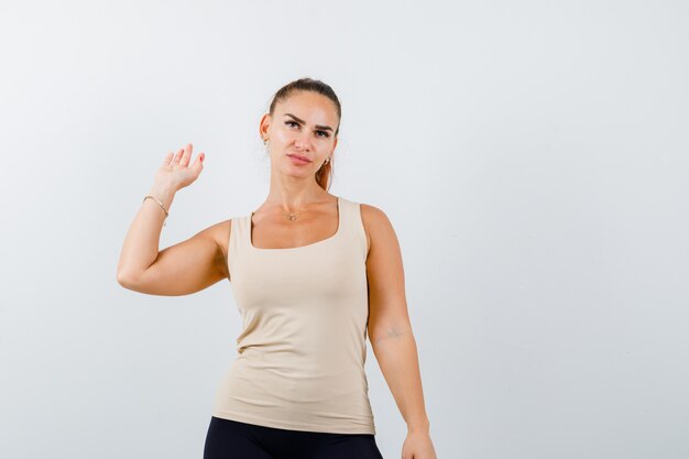 Giovane donna agitando la mano per il saluto in canottiera beige e guardando fiducioso