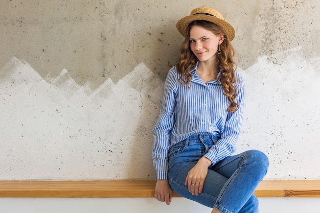 Giovane donna alla moda attraente che si siede alla parete