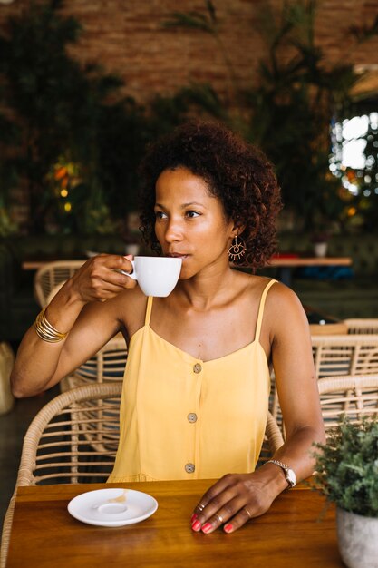 Giovane donna alla moda che si siede nel caffè bevente del caffè