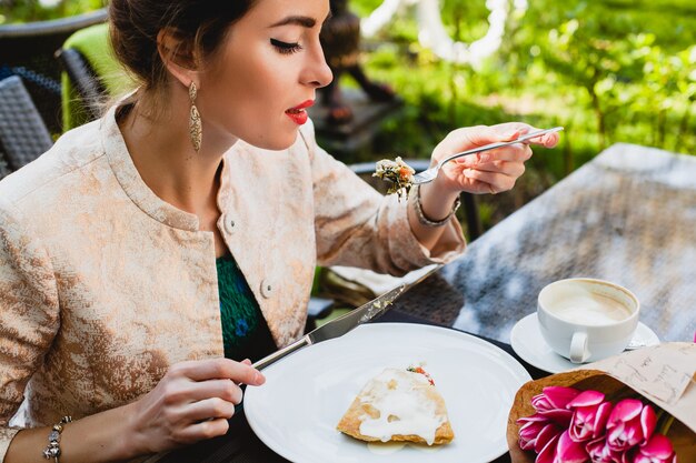 Giovane donna alla moda che si siede nella caffetteria, mangiando una gustosa torta