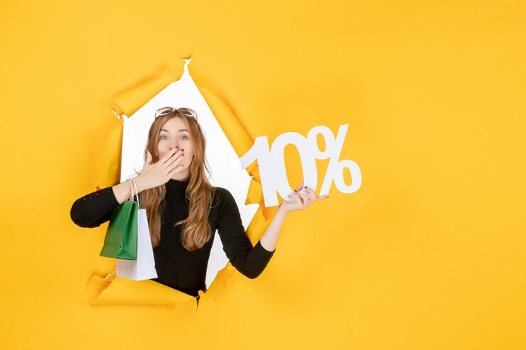 Foto gratuito giovane donna alla moda che tiene in mano le borse della spesa e la percentuale di sconto attraverso il foro di carta strappata nel muro