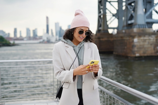 Giovane donna alla moda che utilizza smartphone all'aperto mentre esplora la città