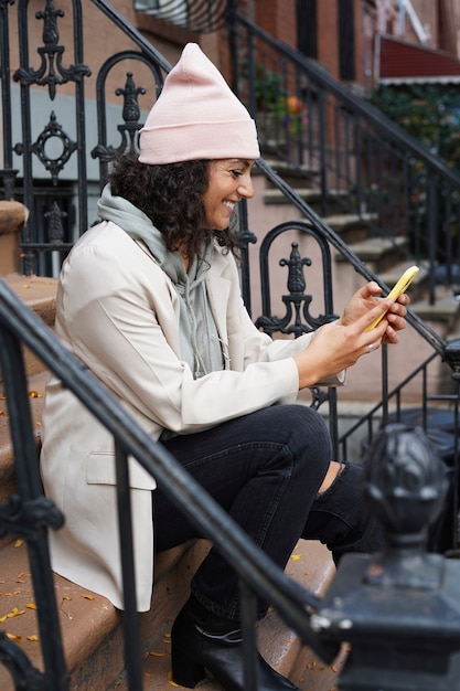 Giovane donna alla moda che utilizza smartphone mentre è seduta nelle steppe in città