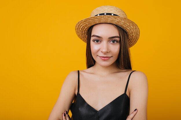 Giovane donna alla moda con grandi occhi marroni in posa con un sorriso delicato. Ritratto dell'interno della meravigliosa ragazza europea indossa un cappello di paglia alla moda.