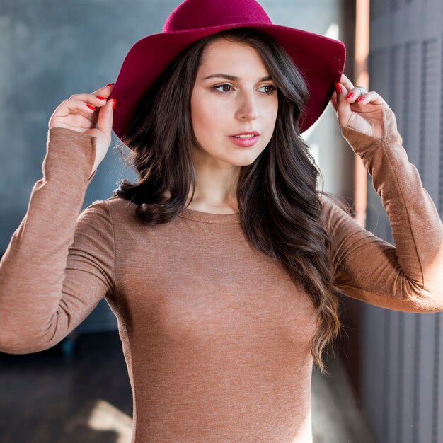 Giovane donna alla moda con i capelli lunghi che indossa il cappello rosa sulla sua testa