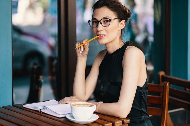 Giovane donna alla moda con i vetri alla moda che si siedono alla tavola