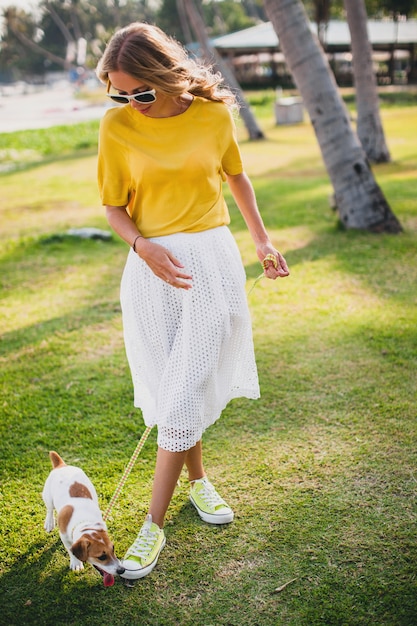 Giovane donna alla moda hipster che tiene camminare e giocare con il cane in spiaggia