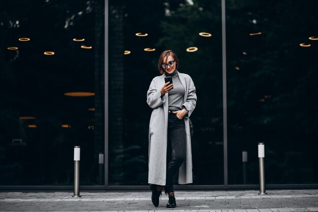 Giovane donna alla moda in cappotto grigio, parlando al telefono