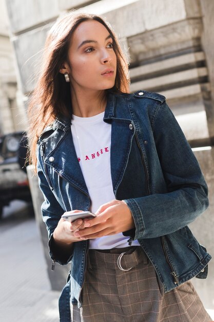 Giovane donna alla moda in giacca di jeans utilizzando smartphone